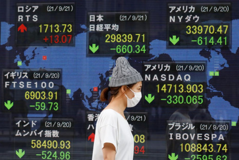 A woman wearing a protective mask, amid the COVID-19 outbreak, walks past an electronic board displaying Japan and other countries' stock indexes outside a brokerage in Tokyo, Japan, September 21, 2021. 
