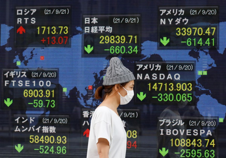 A woman wearing a protective mask, amid the COVID-19 outbreak, walks past an electronic board displaying Japan and other countries' stock indexes outside a brokerage in Tokyo, Japan, September 21, 2021. 