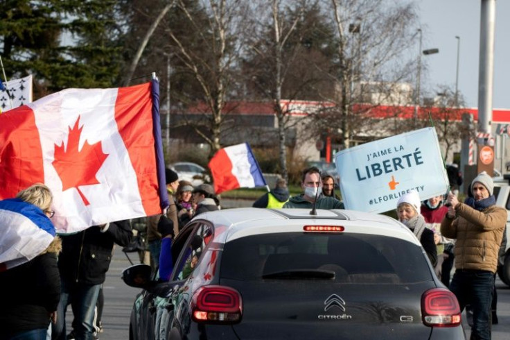 French protesters wave Canadian and French flags. The French 'freedom convoy' is one of several worldwide inspired by a truckers' standoff with authorities in Canada
