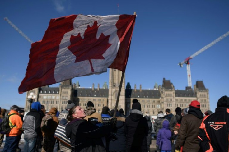 A demonstrator lifts a Canadian flag after praying during a protest by truck drivers outside the Canadian parliament in Ottawa on February 15, 2022