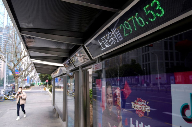 A man wearing a mask walks by an electronic board showing the Shanghai and Shenzhen stock indexes in Shanghai, China, February 3, 2020.