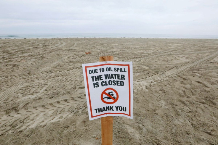 A sign indicating that the beach is closed is seen as workers rake up crude oil, after more than 3,000 barrels (126,000 gallons) of crude oil leaked from a ruptured pipeline into the Pacific Ocean in Newport Beach, California, U.S., October 7, 2021.