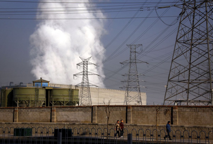 Pedestrians walk along a footpath in front of a massive chimney billowing smoke for a coal-burning power station in central Beijing January 12, 2012.