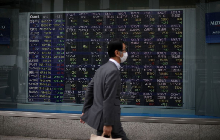 A man wearing protective face mask, following an outbreak of the coronavirus disease (COVID-19), walks in front of a stock quotation board outside a brokerage in Tokyo, Japan, March 10, 2020. 