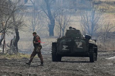 A service member of pro-Russian troops in a uniform without insignia walks next to an armoured vehicle with symbols "Z" painted on its side in the separatist-controlled village of Bugas during Ukraine-Russia conflict in the Donetsk region, Ukraine March 6
