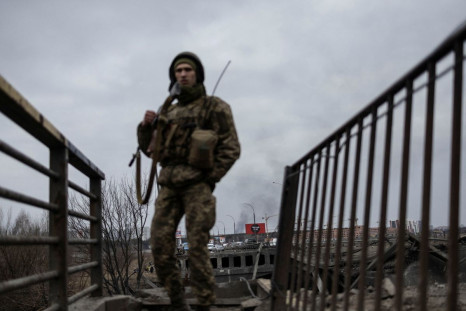 Smoke rises as a service member of the Ukrainian armed forces stands by the only escape route used by locals to evacuate from the town of Irpin, after days of heavy shelling, while Russian troops advance towards the capital, in Irpin, near Kyiv, Ukraine M