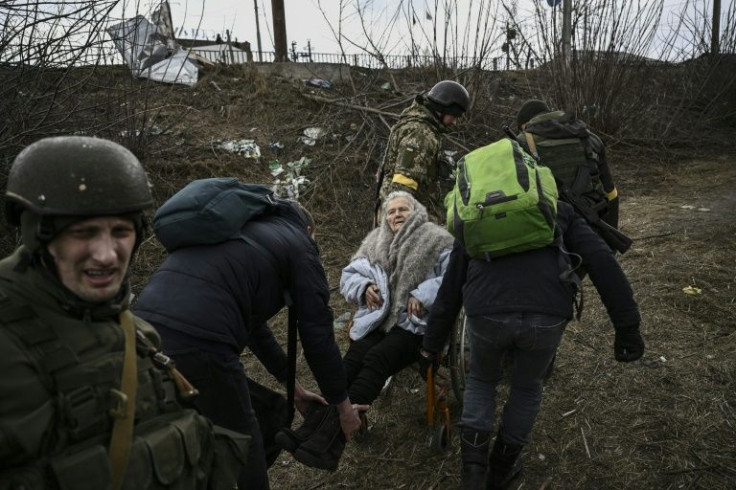 People help an elderly woman in a wheelchair flee the city of Irpin, west of Kyiv