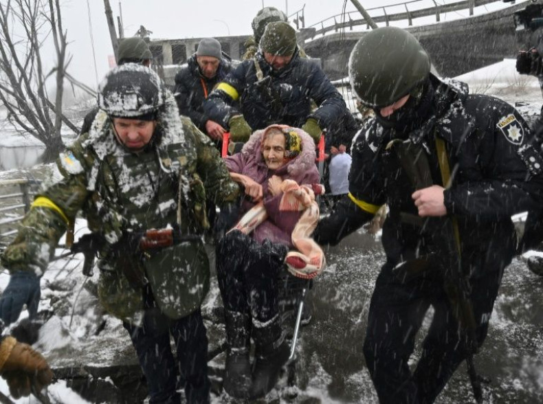 Ukrainian soldiers help an elderly woman to cross a destroyed bridge as she evacuates the city of Irpin, northwest of Kyiv, on March 8, 2022