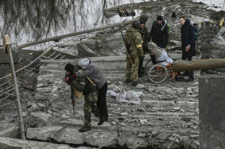 People waited in a long line to cross over the Irpin river on makeshift walkways of planks and mangled metal