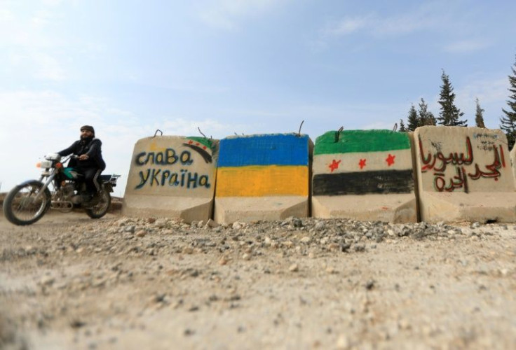 A man rides a motorcycle past cement blocks bearing flags of Ukraine and the Syrian opposition near the rebel-held city of Al-Bab in the northern province of Aleppo