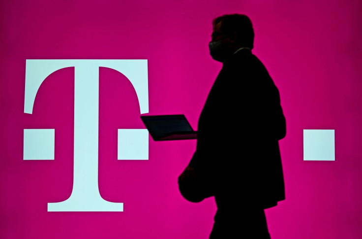 FILE PHOTO:A man carrying his computer passes by the logo of German telecommunication company "Deutsche Telekom" at the ITS World Congress 2021, a fair for intelligent transport systems, in Hamburg, Germany, October 13, 2021.