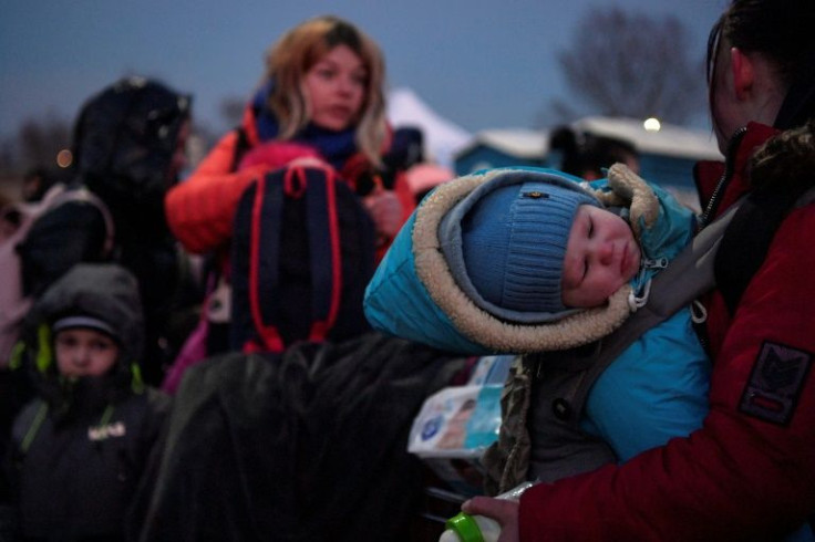 A child is carried by a woman as refugees from Ukraine proceed to a gathering point after entering Poland at the Medyka border crossing