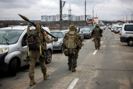 Ukrainian servicemen carry rocket-propelled grenades and sniper rifles as they walk towards the city of Irpin, northwest of Kyiv, on March 13, 2022