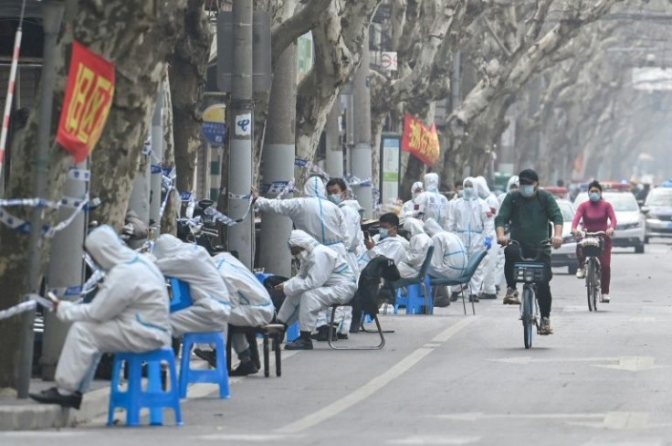 Workers in protective clothing sit near a locked down area after the detection of new cases of Covid-19 in Shanghai on March 14