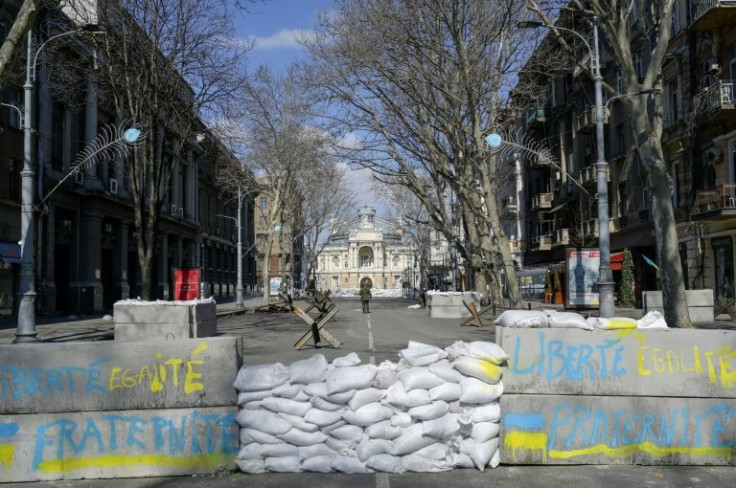 Past a set of barricades, a road is cordoned off with large concrete blocks, with the French national motto "Liberty, equality, fraternity" written in French in yellow and blue, the colours of Ukraine's flag