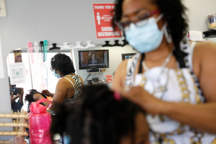 Miracle Williams, braids the hair of a customer at Dimensions In Hair Salon in North Minneapolis, while they watch the second day in the trial of former police officer Derek Chauvin, who is facing murder charges in the death of George Floyd, in Minneapoli