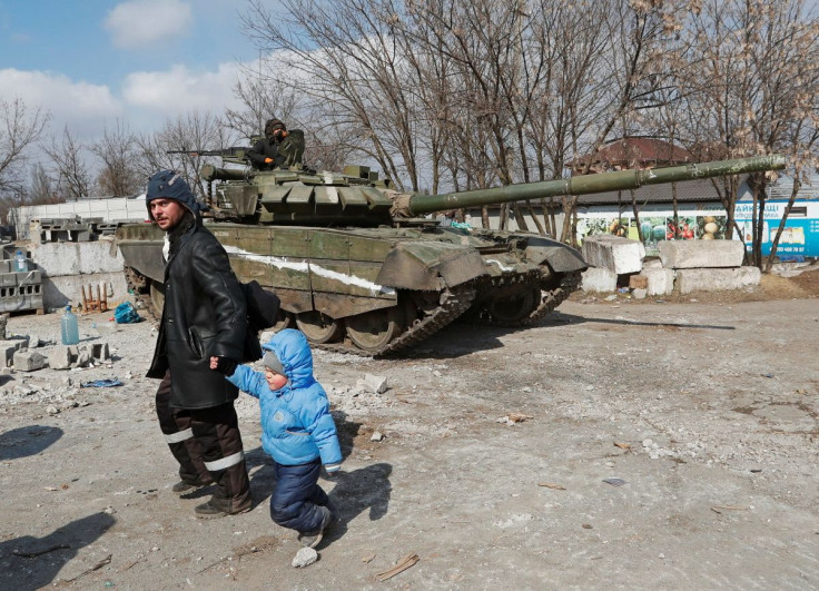 A local resident walks with a child past a tank of pro-Russian troops during Ukraine-Russia conflict in the besieged southern port city of Mariupol, Ukraine March 18, 2022. 