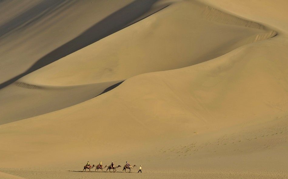 Tourists ride camels on the Mingsha Sand Dunes during a visit to Crescent Moon Spring on the outskirts of Dunhuang