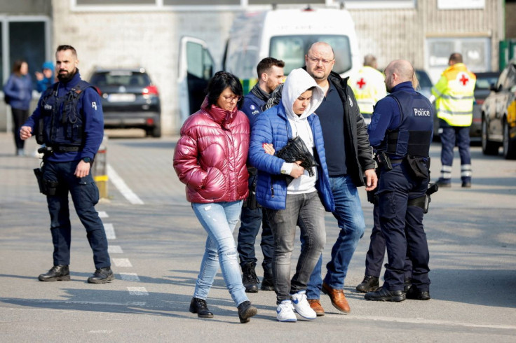 People walk as police officers keep guard near the site where a vehicle drove into a group of Belgian carnival performers who were preparing for a parade in the village of Strepy-Bracquegnies, Belgium March 20, 2022.