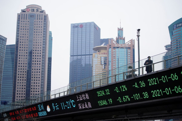 A man wearing a face mask, following the coronavirus disease (COVID-19) outbreak, stands on an overpass with an electronic board showing Shanghai and Shenzhen stock indexes, at the Lujiazui financial district in Shanghai, China January 6, 2021. 