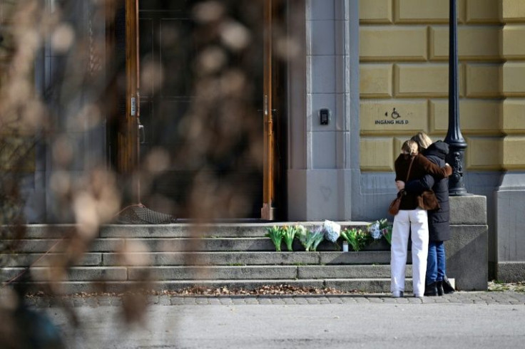 Bouquets of flowers lie on stairs as people hug outside the Malmo Latin School after the deadly attack