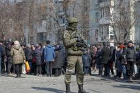 A Russian army soldier stands next to local residents who queue for humanitarian aid delivered during Ukraine-Russia conflict, in the besieged southern port of Mariupol, Ukraine March 23, 2022.  