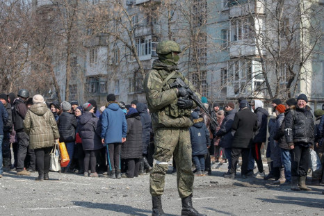 A Russian army soldier stands next to local residents who queue for humanitarian aid delivered during Ukraine-Russia conflict, in the besieged southern port of Mariupol, Ukraine March 23, 2022.  