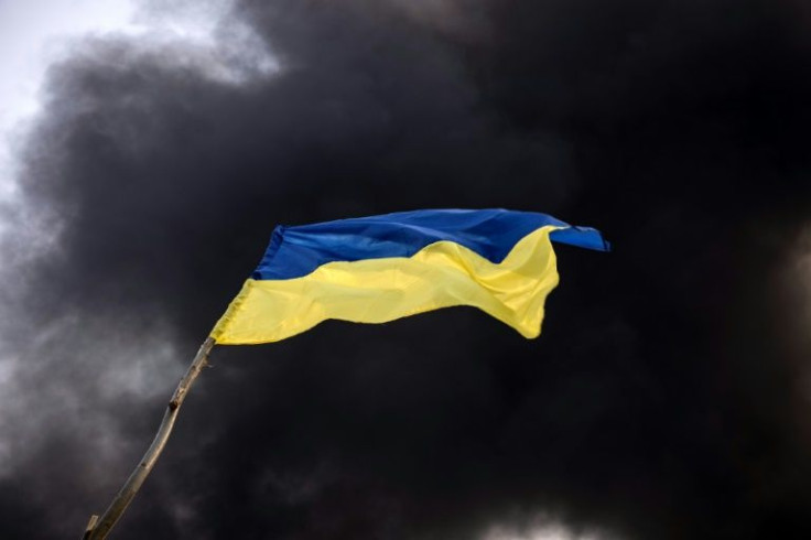 Smoke rises behind a Ukrainian flag after Russian attacks hit a fuel storage facility in the city of Kalynivka