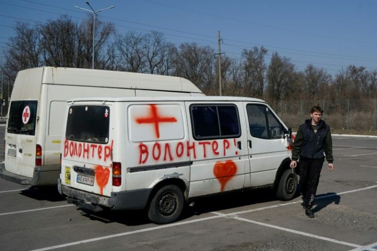 A volunteer walks by a vehicle labeled 'volunteers', carrying medicines to civilians who are trapped in Mariupol