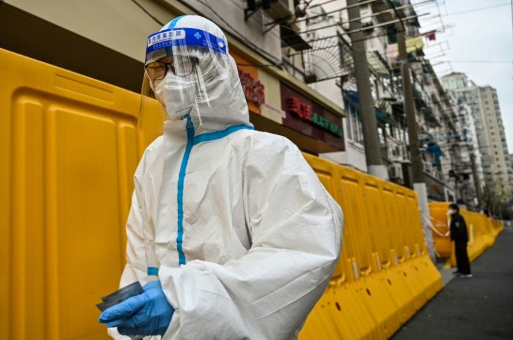 A worker in protective gear walks next to barriers separating a street from buildings in lockdown in Shanghai's Jing'an district