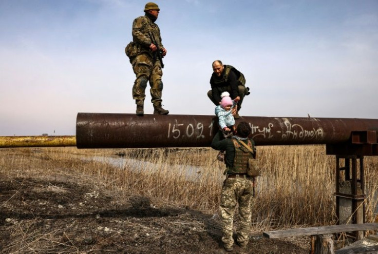 Ukrainian soldiers help three-year-old Karolina Tkachenko across a long, narrow pipeline on the frontline east of Kyiv