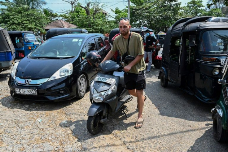A tourist pushes his scooter to stand in a queue to fill fuel at a fuel station