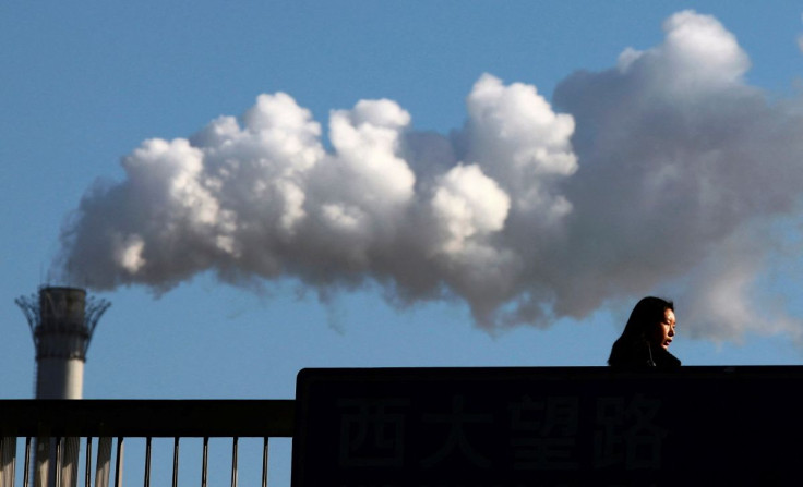 A woman walks across a bridge in front of a chimney billowing smoke from a coal-burning power station in central Beijing February 25, 2011.