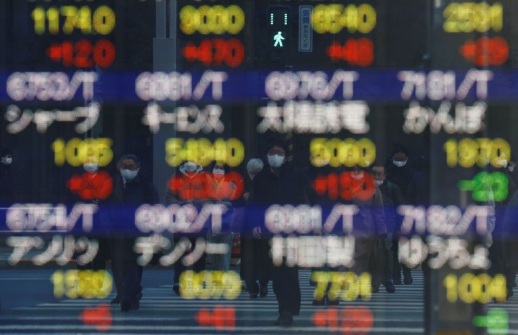 Pedestrians wearing protective masks, amid the coronavirus disease (COVID-19) outbreak, are reflected on an electronic board displaying various companyâs stock prices outside a brokerage in Tokyo, Japan, February 25, 2022. 
