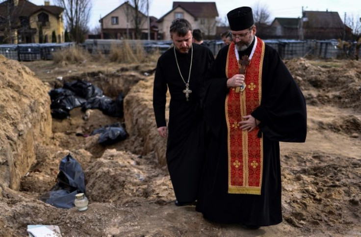 Priests pray over a mass grave on the grounds of St Andrew church in the Ukrainian town of Bucha, where authorities have launched an investigation of civilian deaths uncovered after Russian troops withdrew