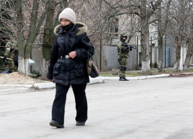 A woman walks along a street past servicemen of pro-Russian militia in Stanytsia Luhanska in the Luhansk region, Ukraine February 27, 2022. 