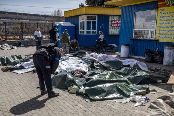 A Ukrainian police officer bends over bodies covered with tarpaulin after the rocket attack in Kramatorsk, eastern Ukraine