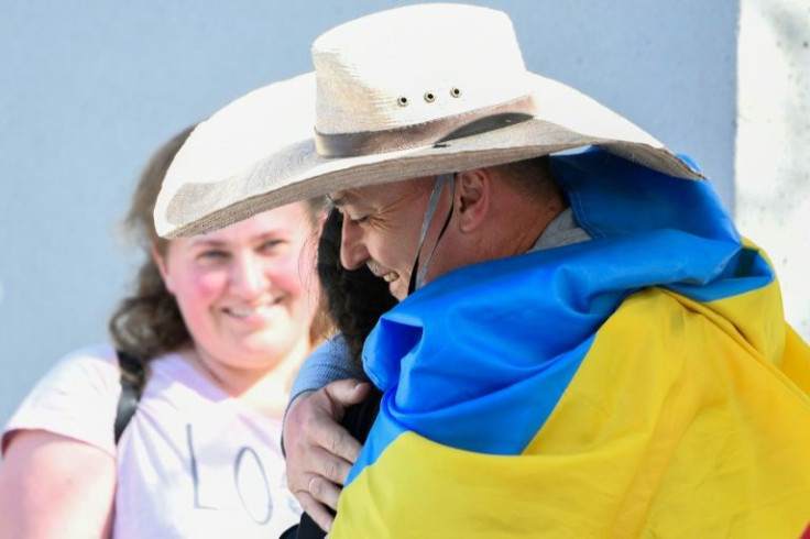 Oleksii Yeromin, wrapped in a Ukrainian flag, hugs a refugee as they cross the San Ysidro PedWest port of entry along the US-Mexico border between Tijuana, Baja California, and the US on April 8, 2022 in San Ysidro, California