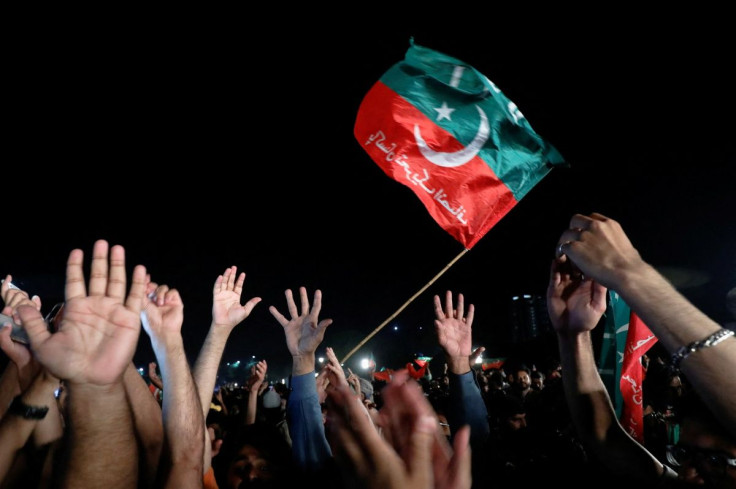 A flag of the Pakistan Tehreek-e-Insaf (PTI) political party is seen as the party's supporters raise hands during a rally in support of former Pakistani Prime Minister Imran Khan, after he lost a confidence vote in the lower house of parliament, in Islama