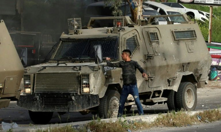 A Palestinian man hurls stones from behind an Israeli security armoured vehicle during a raid to look for wanted Palestinians in Nablus city, in the occupied West Bank