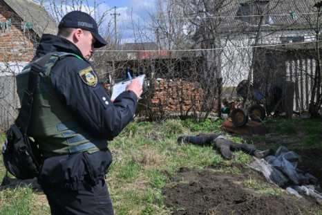 A policeman fills out paperwork next to the body of a civilian man buried in the yard of his house after his was exhumed in Andriivka village, Kyiv region, on April 11, 2022