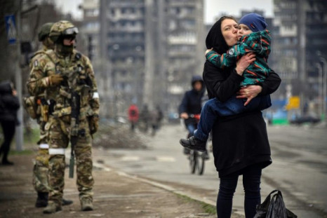 A woman holds and kisses a child next to Russian soldiers in a street of Mariupol on April 12, 2022, as Russian troops intensify a campaign to take the strategic port city