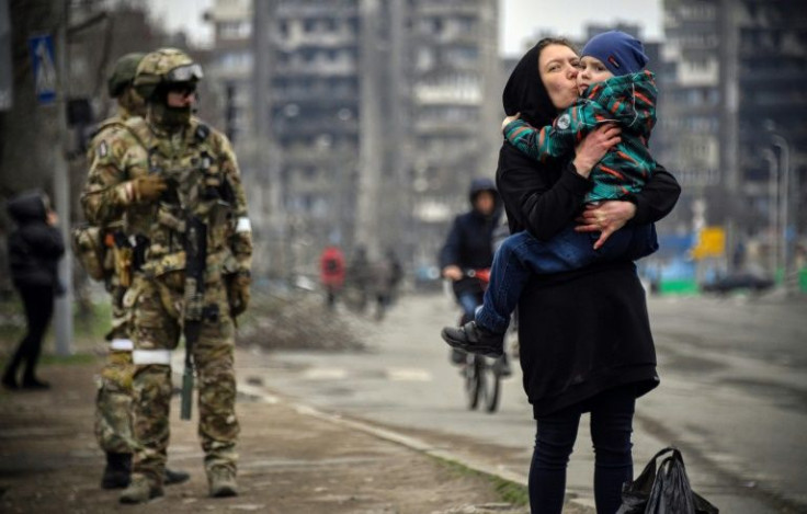 A woman holds and kisses a child next to Russian soldiers in a street of Mariupol on April 12, 2022, as Russian troops intensify a campaign to take the strategic port city