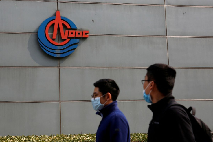 Men wearing face masks walk past a sign of China National Offshore Oil Corp (CNOOC) outside its headquarters in Beijing, China March 8, 2021. 