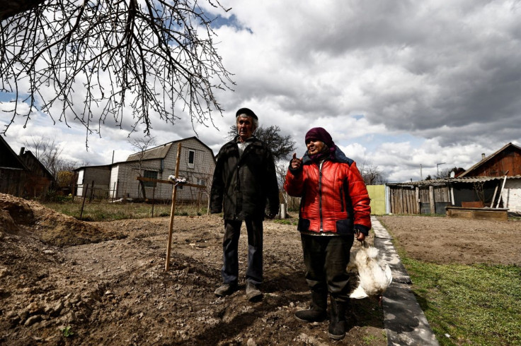 Zinaida Makishaiva, 82, who survived the Russian occupation, stands with Volodymyr Maksuta, 62, beside the grave of their neighbour, Yurii Ostapchuk, who they say was killed by Russian troops while he was trying to extinguish a fire after Russian soldiers