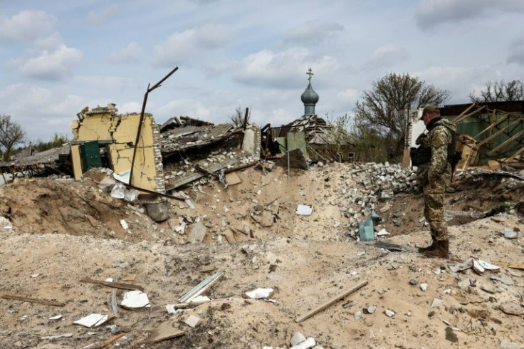 A Ukranian serviceman looks into a crater outside a destroyed home in the village of Yatskivka, eastern Ukraine