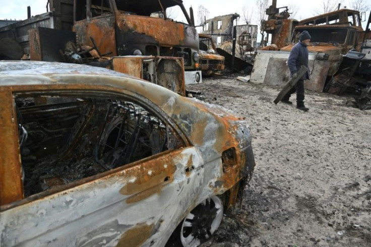 An elderly man carries a board as he walks past destroyed cars in a village near Kyiv