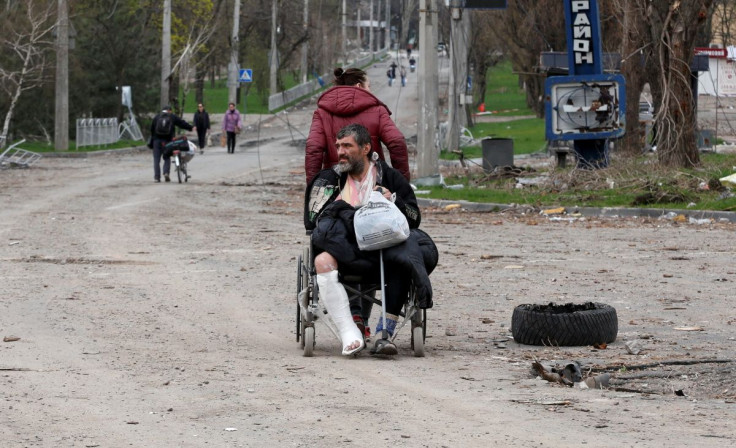 A woman pulls a wheel chair while transporting an injured man in a street in the course of Ukraine-Russia conflict in the southern port city of Mariupol, Ukraine April 18, 2022. 