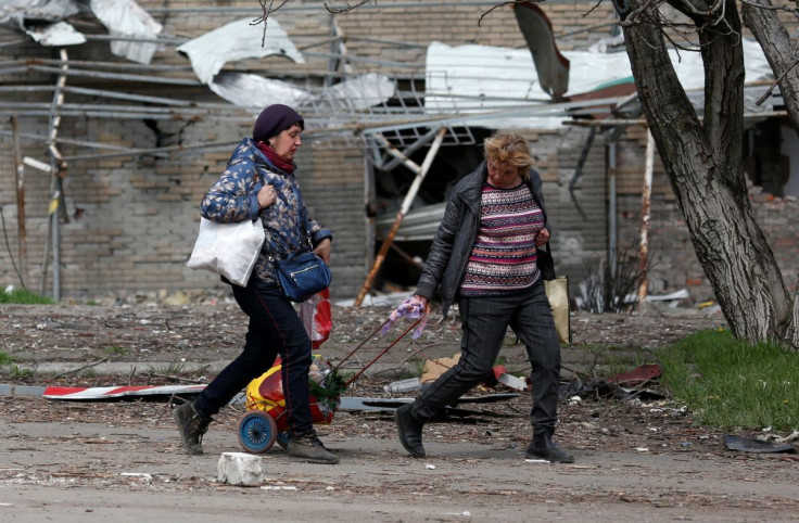 Women walk past a building damaged during Ukraine-Russia conflict in the southern port city of Mariupol, Ukraine April 21, 2022. 
