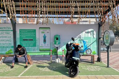 A man checks his mobile phone as he waits while recharging his Ola electric scooter at an electric vehicle charging station in New Delhi, India, February 12, 2022. 
